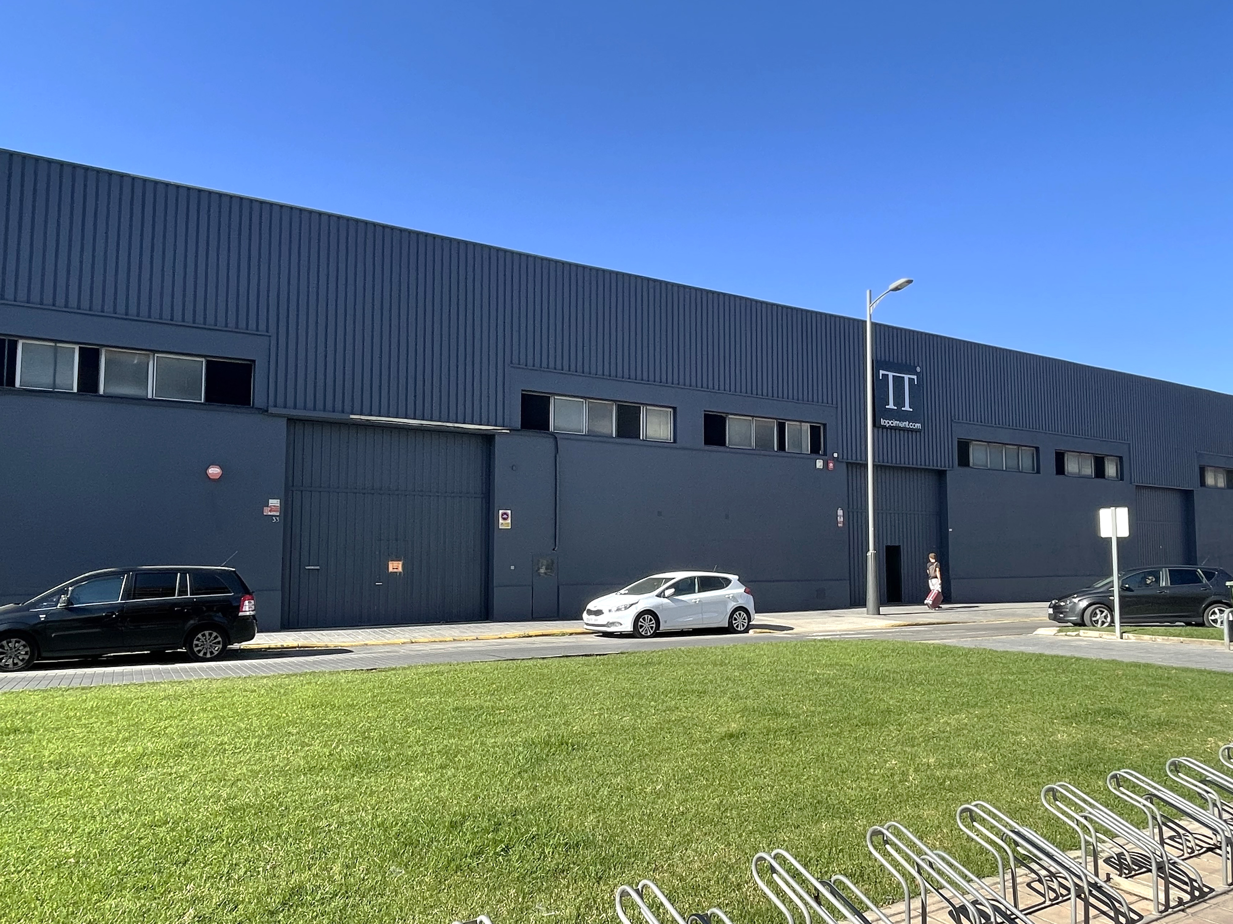 Exterior view of Topciment ®'s industrial buildings, with the logo on the facade, landscaped area in the foreground, and parked vehicles
